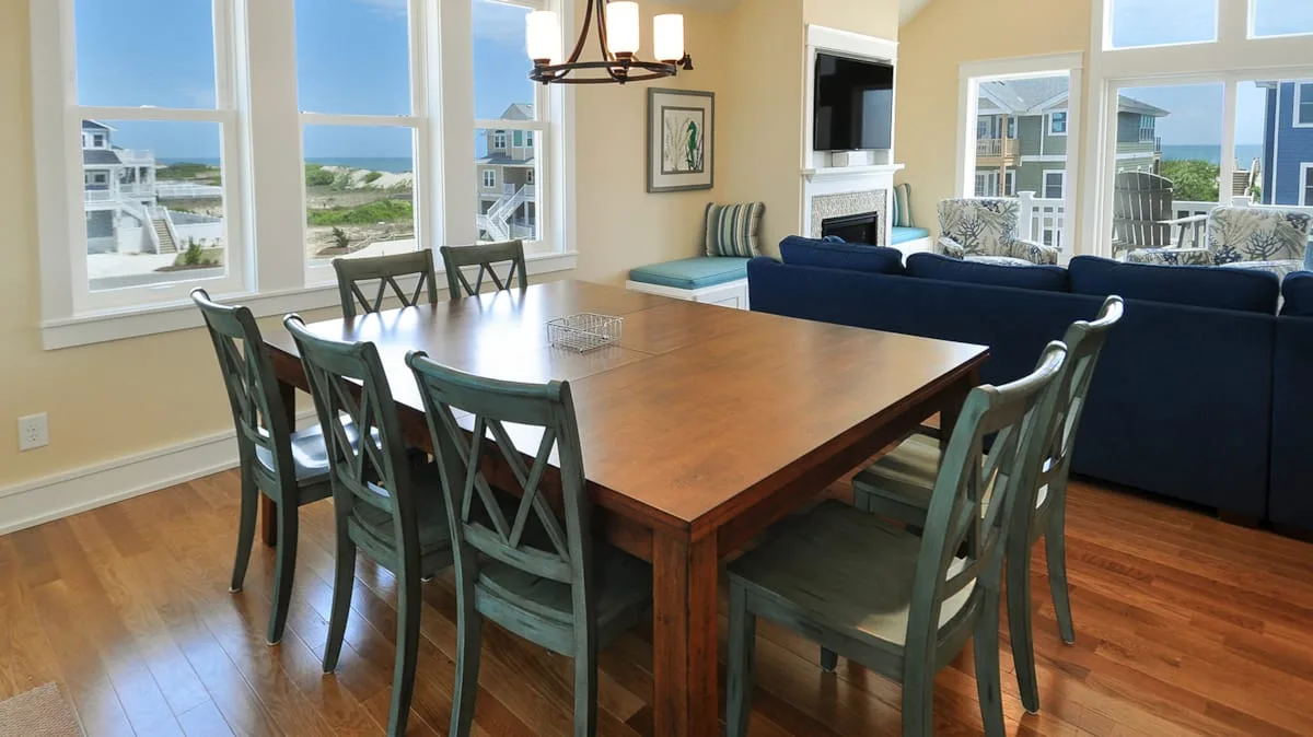 Comedor con una mesa larga de madera y asientos junto a grandes ventanas.