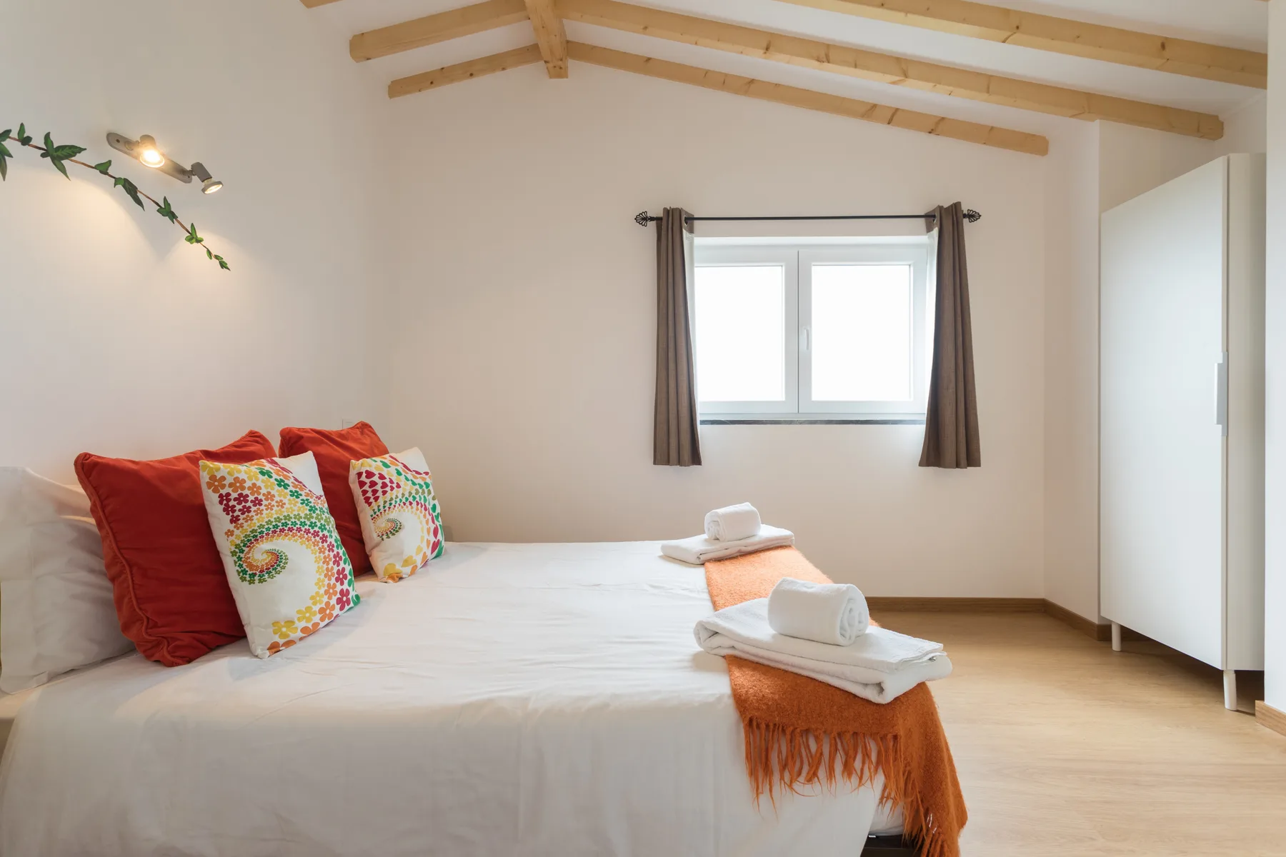 Un dormitorio luminoso con una cama tendida bajo vigas vistas en el techo.