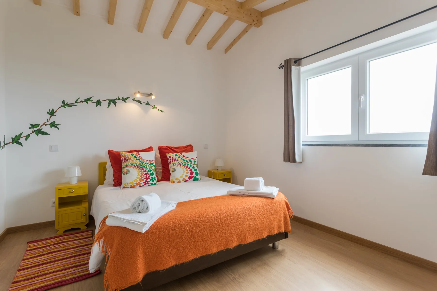 A bedroom with a bed dressed in orange bedding and a large window.