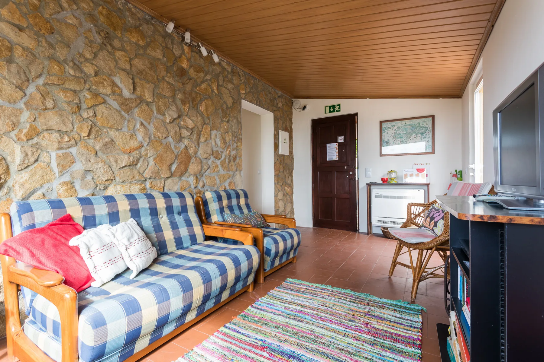 A living room with patterned seating, a stone wall, and a wooden ceiling.
