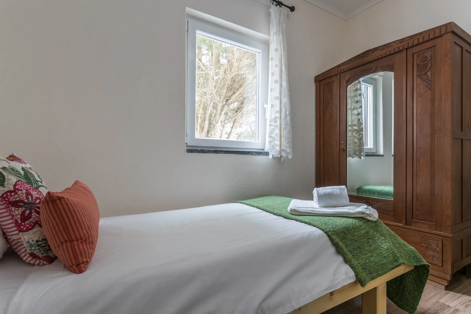 Un dormitorio con una cama, ropa de cama verde y un armario de madera junto a la ventana.