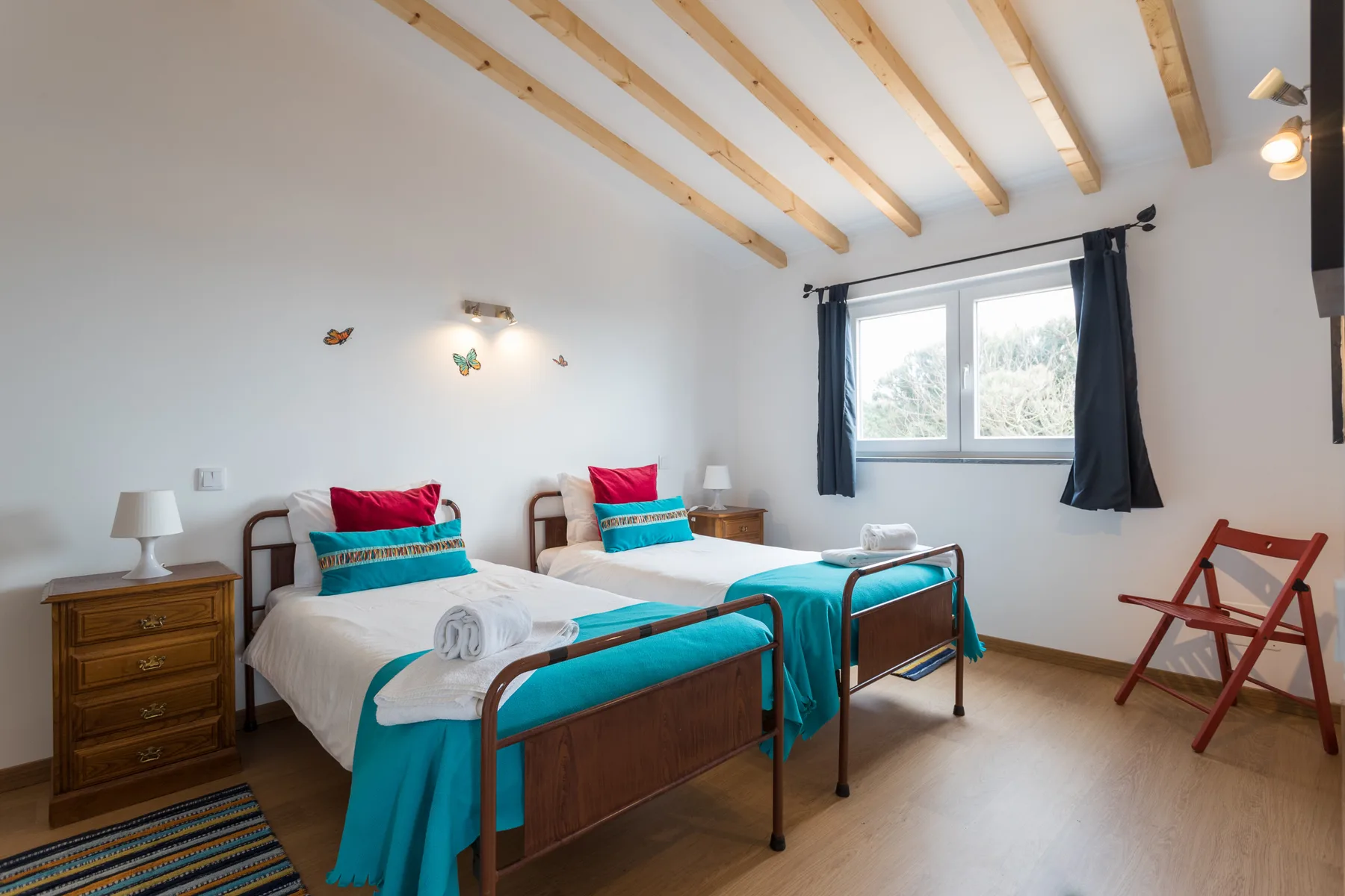 A bright bedroom with two beds dressed in white and turquoise linens.