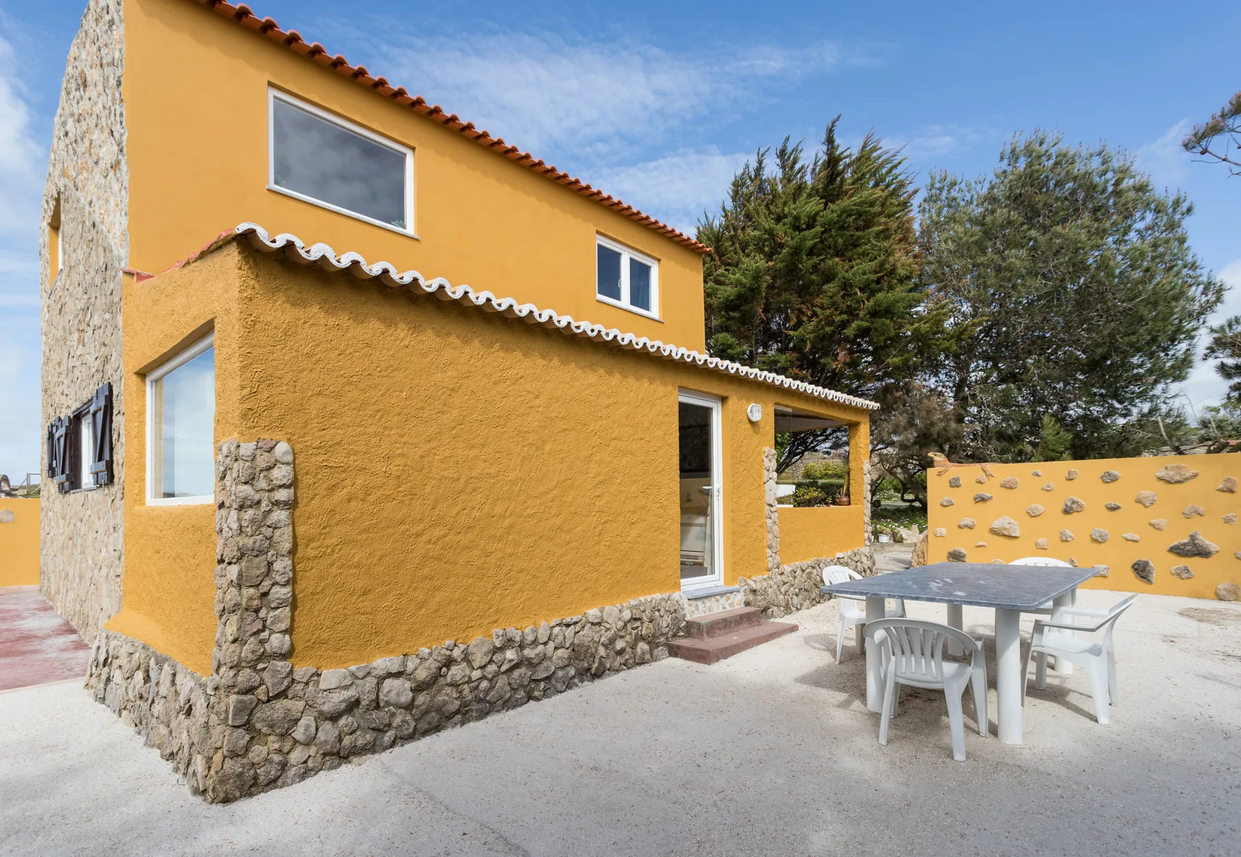 A yellow house with a stone base and an outdoor dining area.
