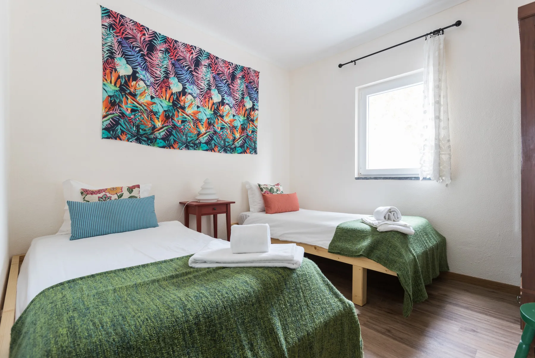 A bedroom with two beds dressed in green covers and colorful wall art.