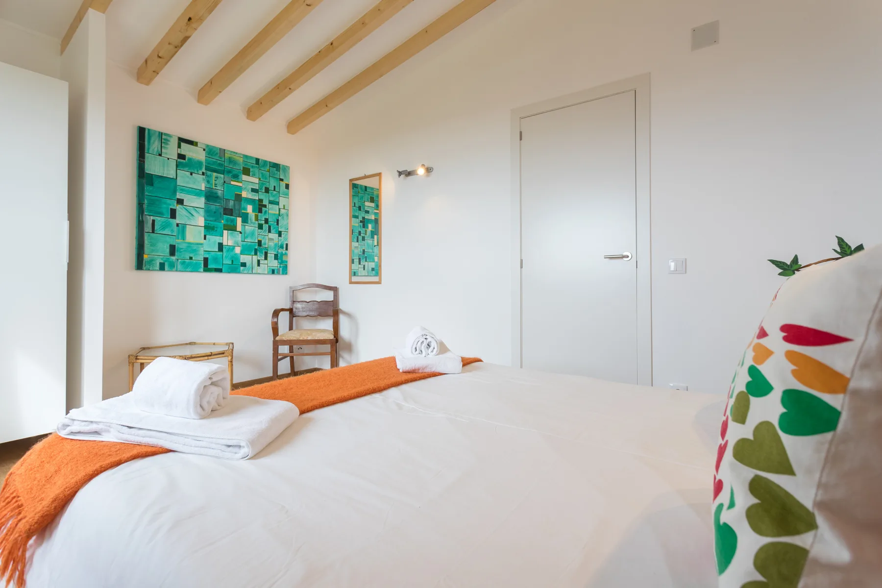 Un dormitorio con una cama, arte mural colorido y vigas de madera a la vista.