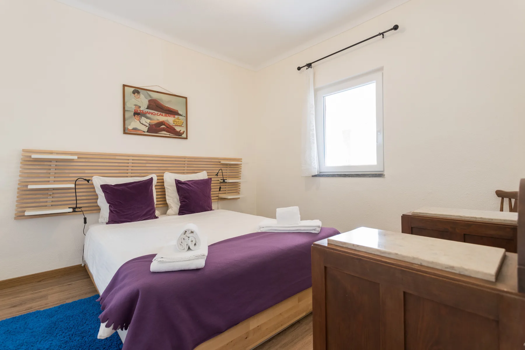 A bedroom with a double bed dressed in white and purple linens.