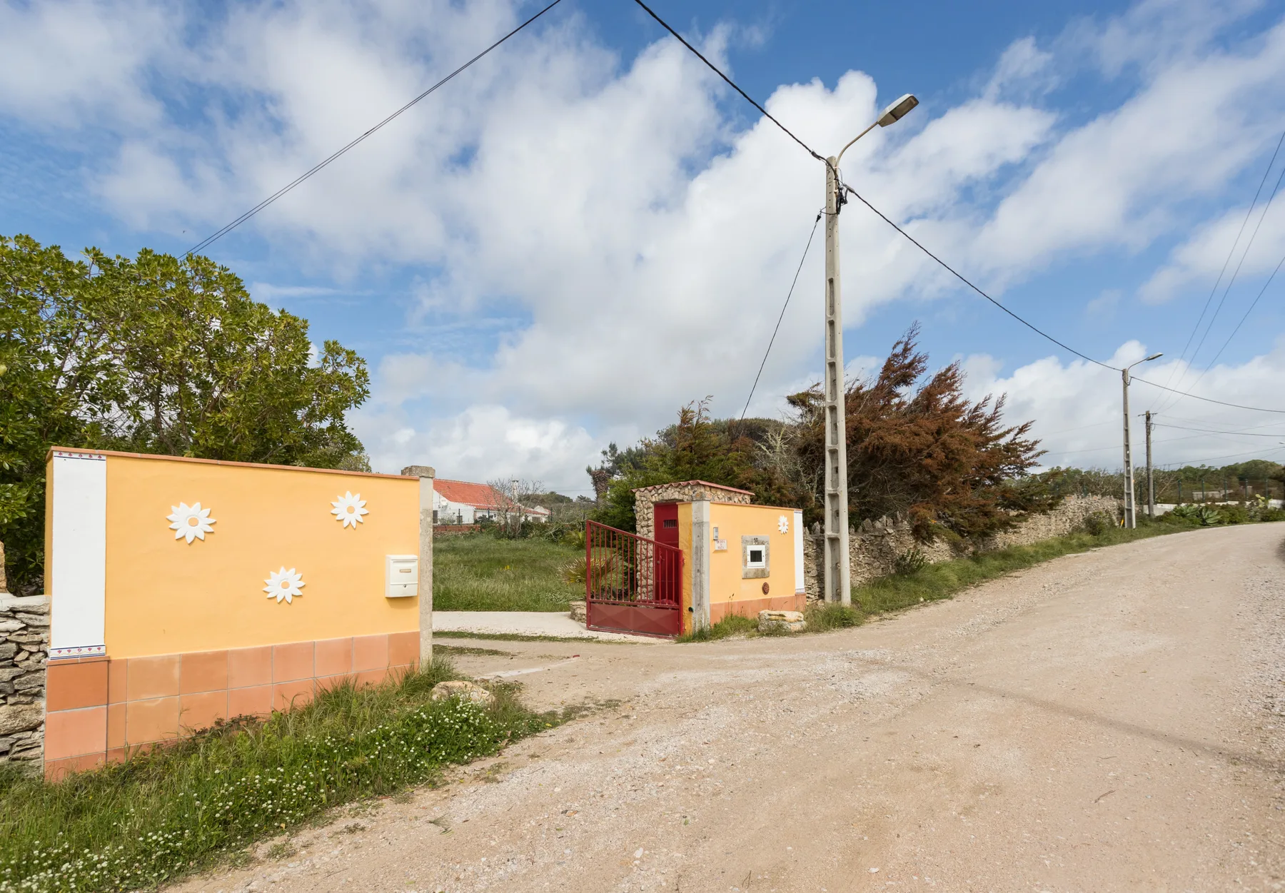 A rural roadside entrance has peach-colored walls and a metal gate beside a dirt road.
