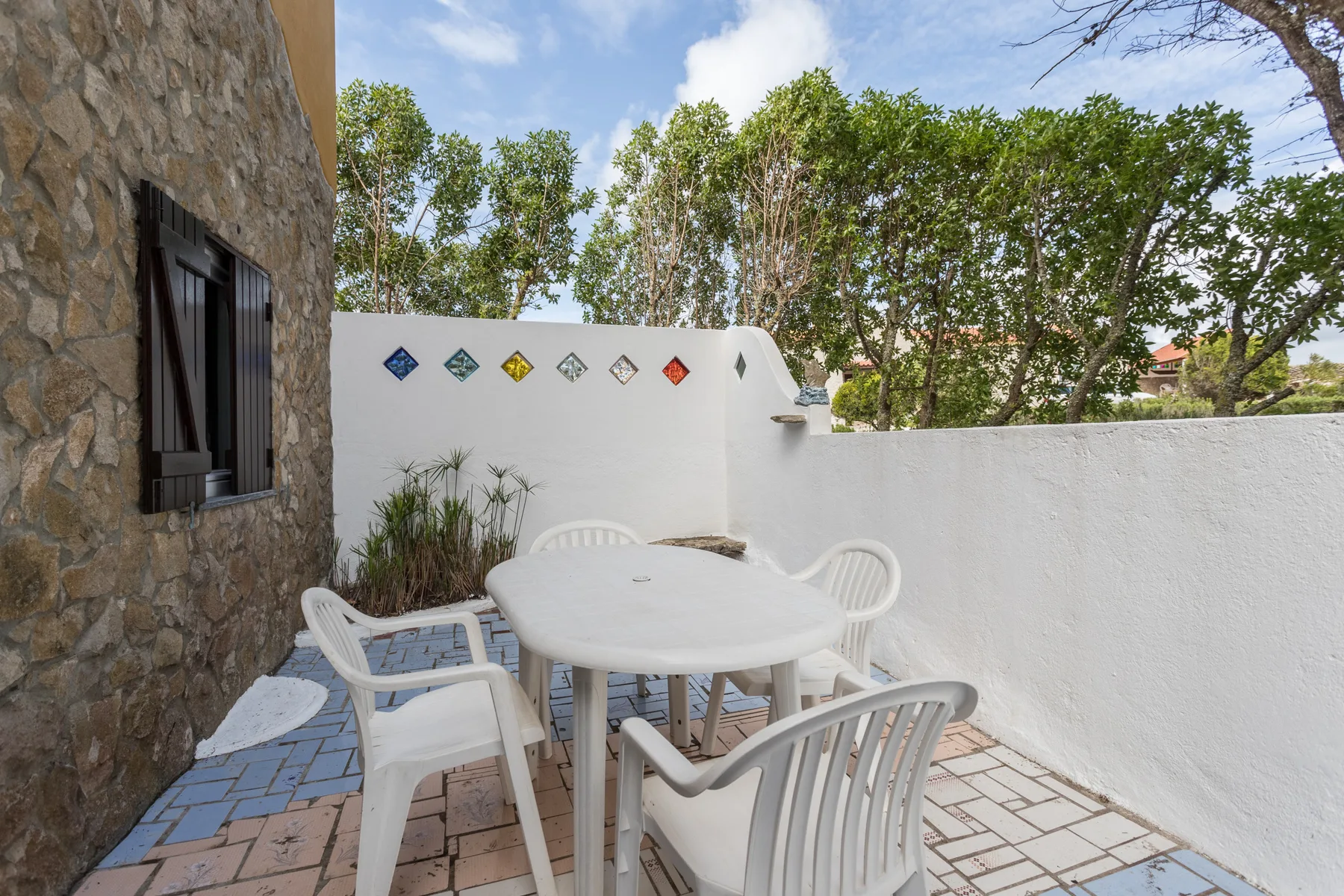 An outdoor patio has a white table and seating beside a stone wall.