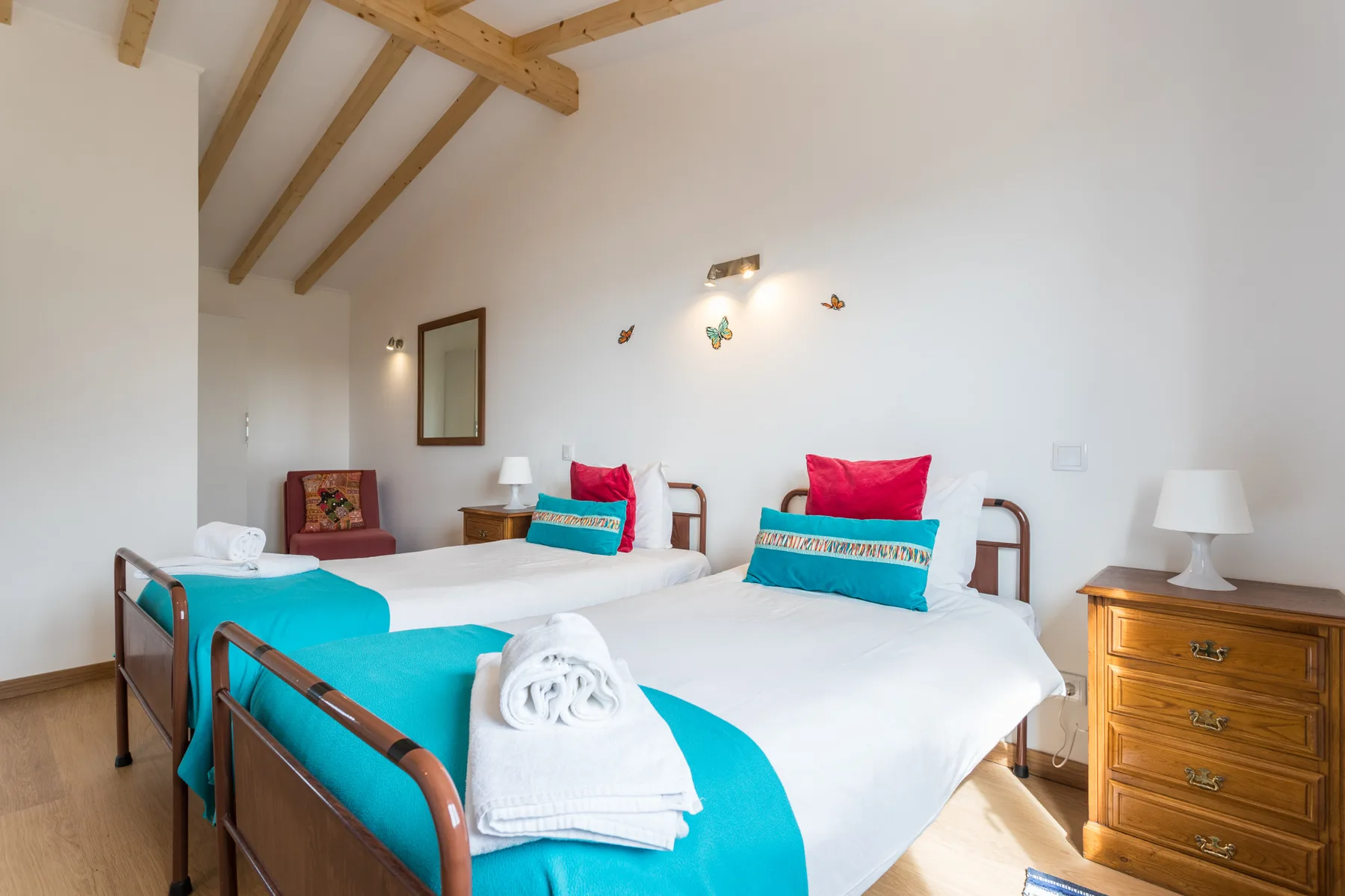 A bright bedroom with two beds dressed in white and turquoise linens.