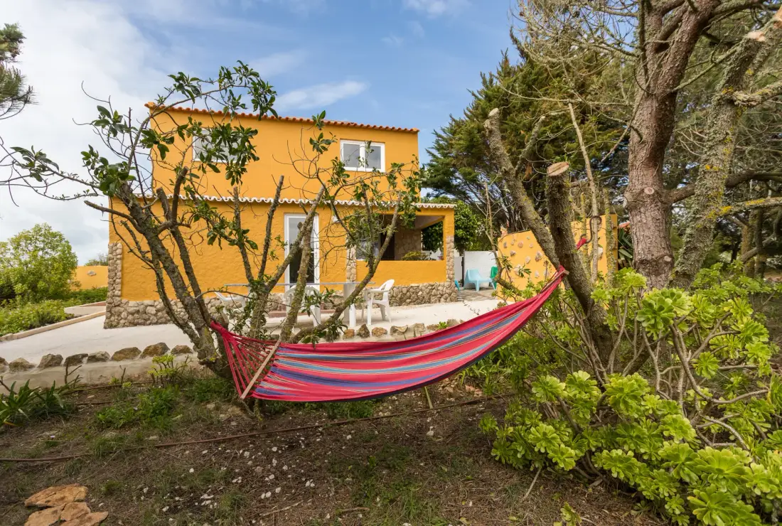 An orange house stands among trees, with a striped hammock in the garden.