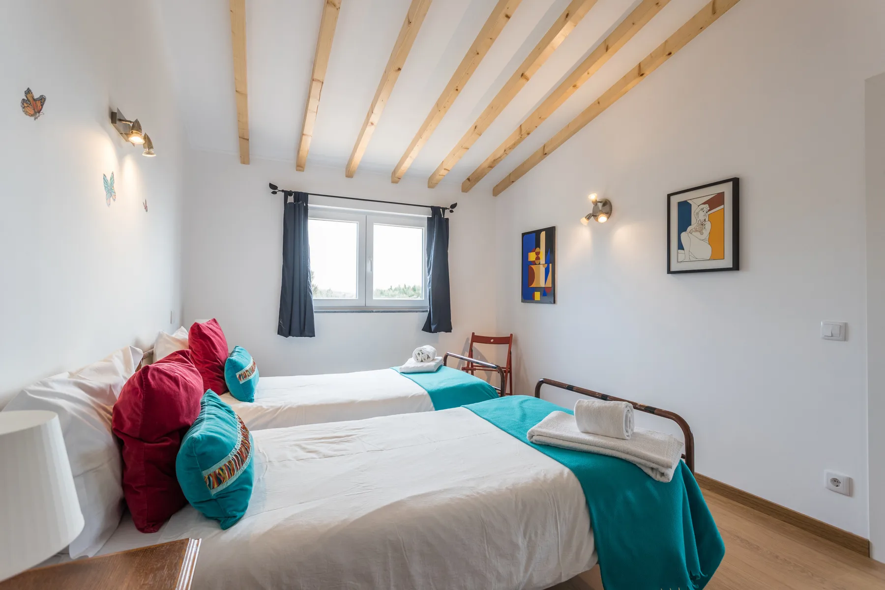 A twin bedroom with white bedding, teal throws, and a window with dark curtains.