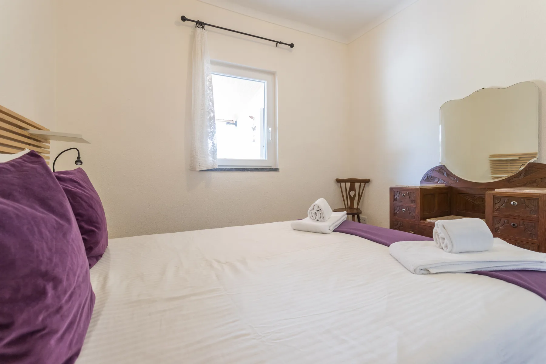Un dormitorio con una cama bien hecha, cojines morados y muebles de madera.