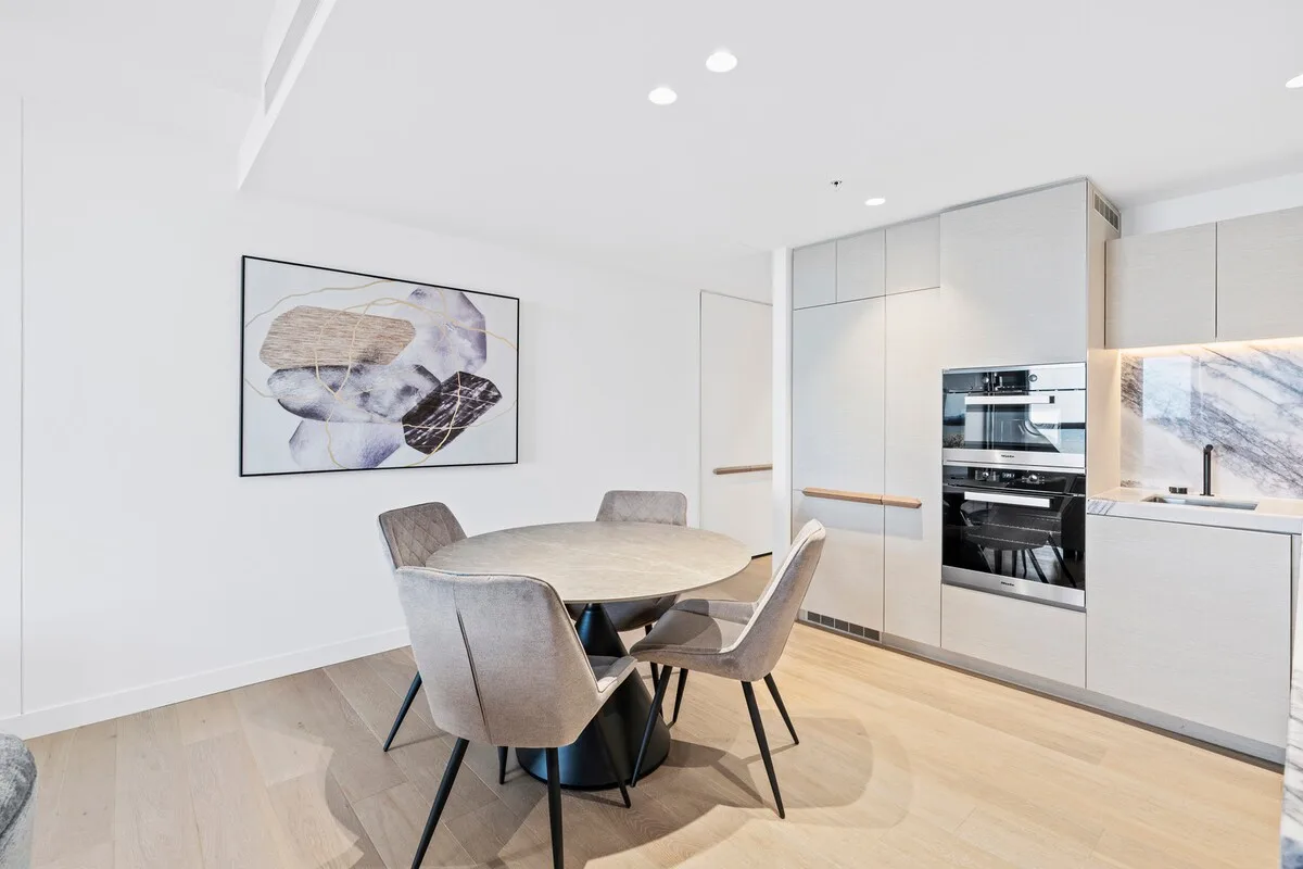Comedor moderno junto a una cocina luminosa, con una mesa redonda y asientos tapizados.