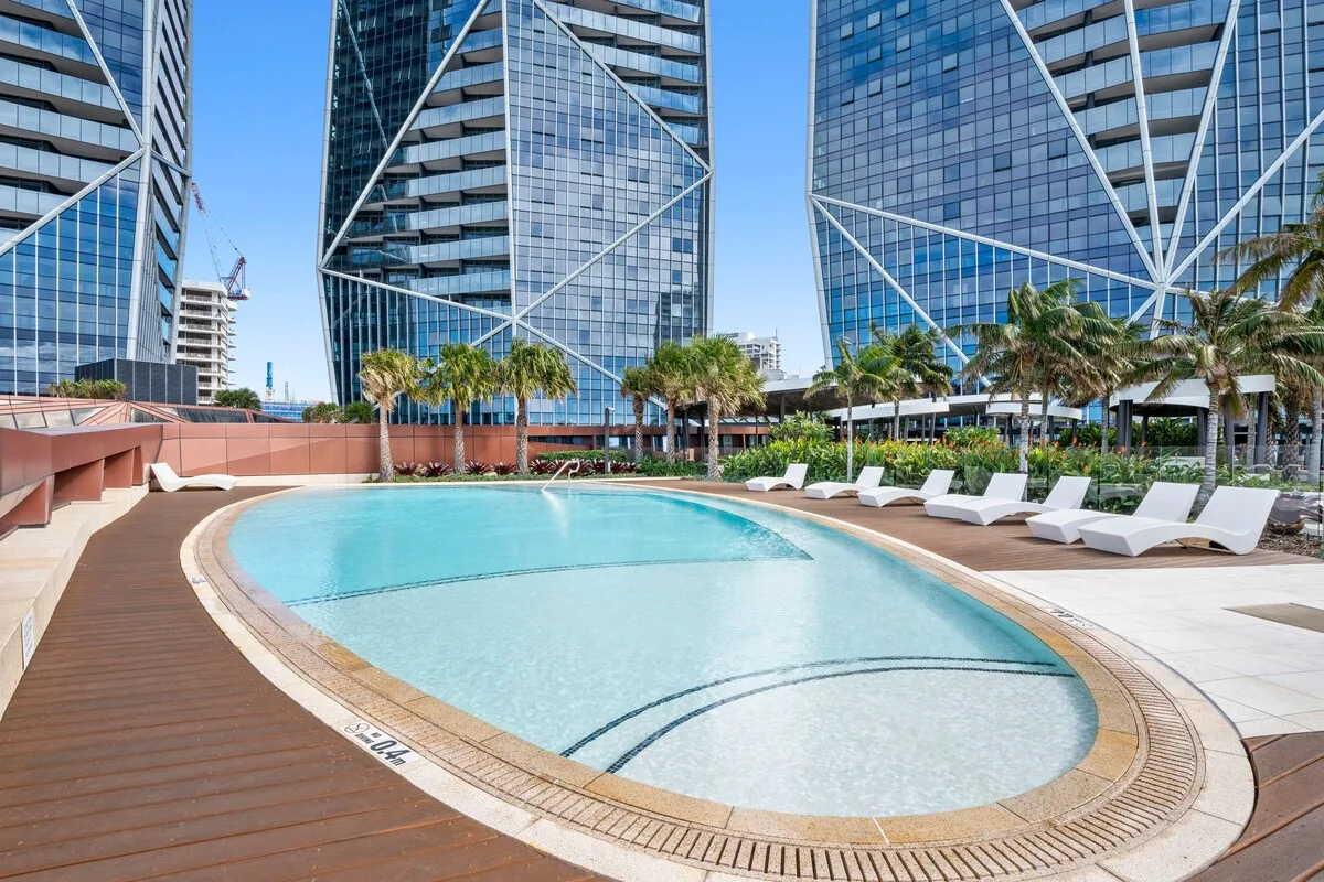 A rooftop pool sits among modern glass buildings and palm trees.