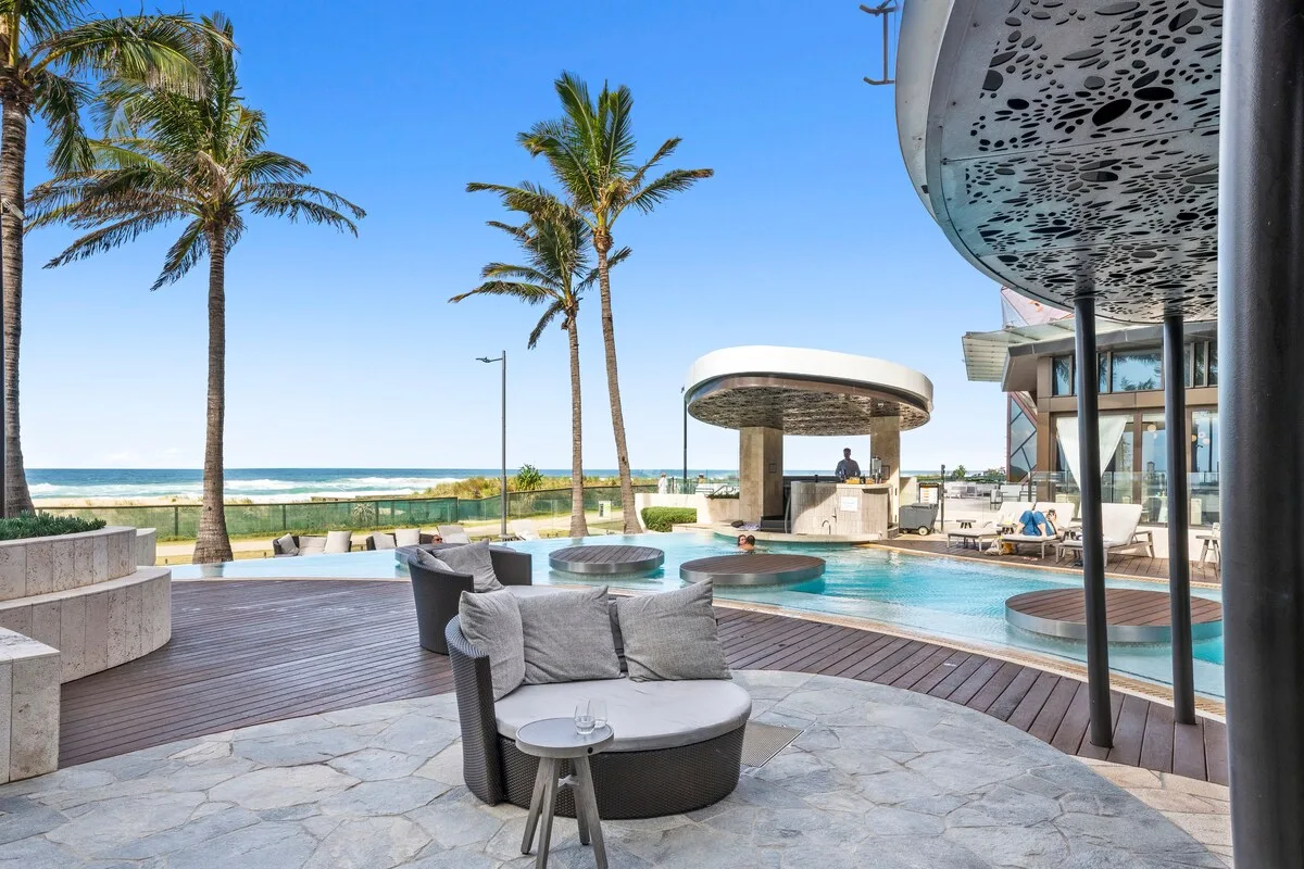 A beachfront pool terrace with curved seating and palm trees.