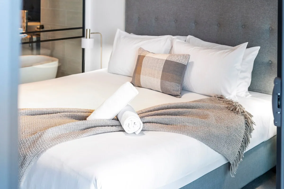 A neatly made bedroom features white bedding and a folded gray throw.