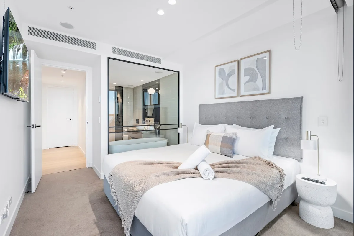 Un dormitorio luminoso con una cama tendida y cuadros enmarcados sobre el cabecero.