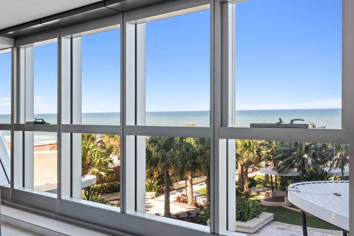 Large windows overlook palm trees, landscaped grounds, and the ocean.
