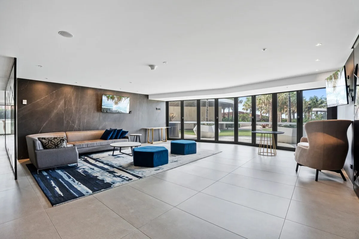 Una sala luminosa con asientos, una alfombra y ventanas de piso a techo.