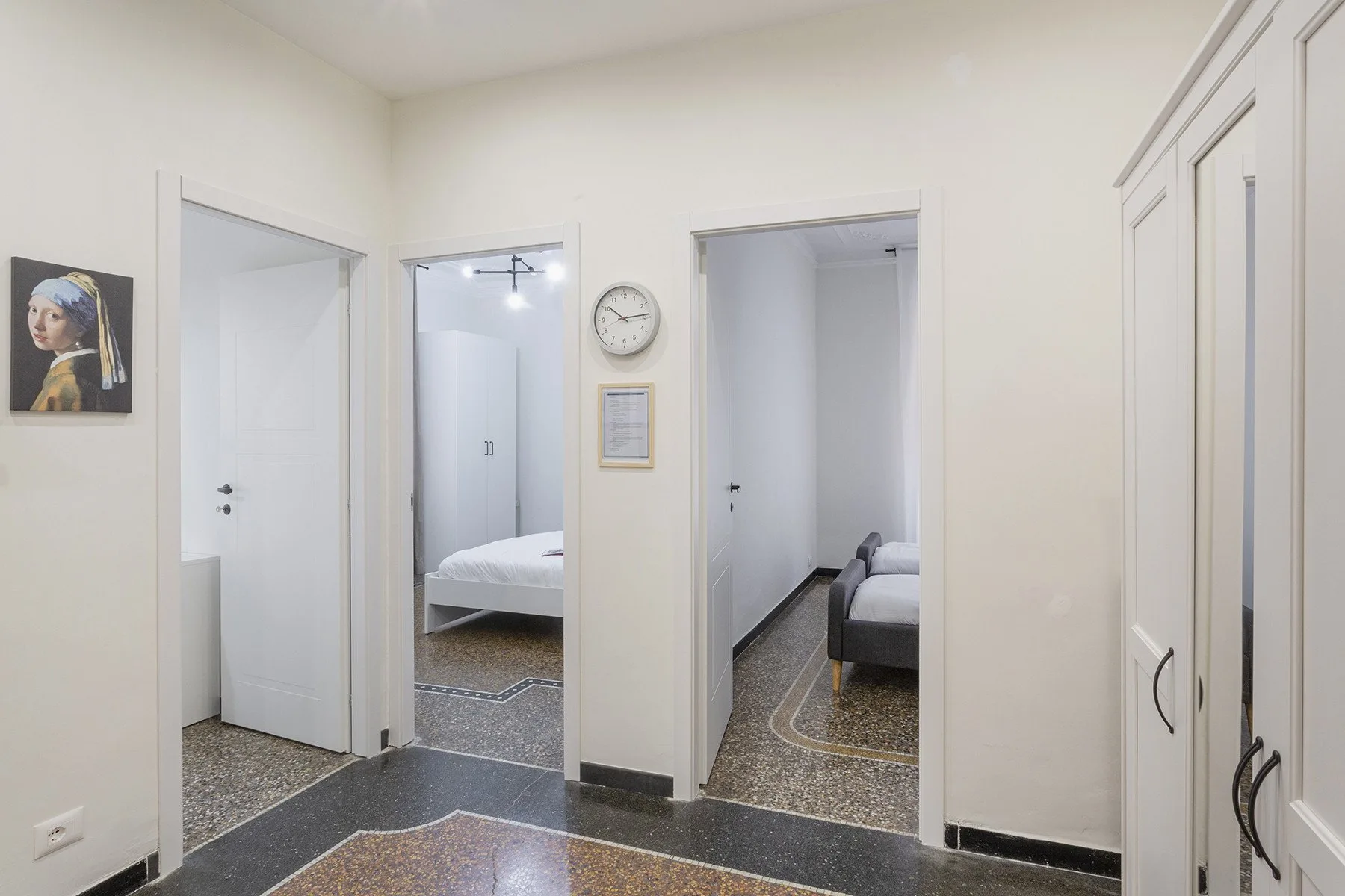 Un pasillo con varias puertas abiertas, arte enmarcado y un reloj de pared.