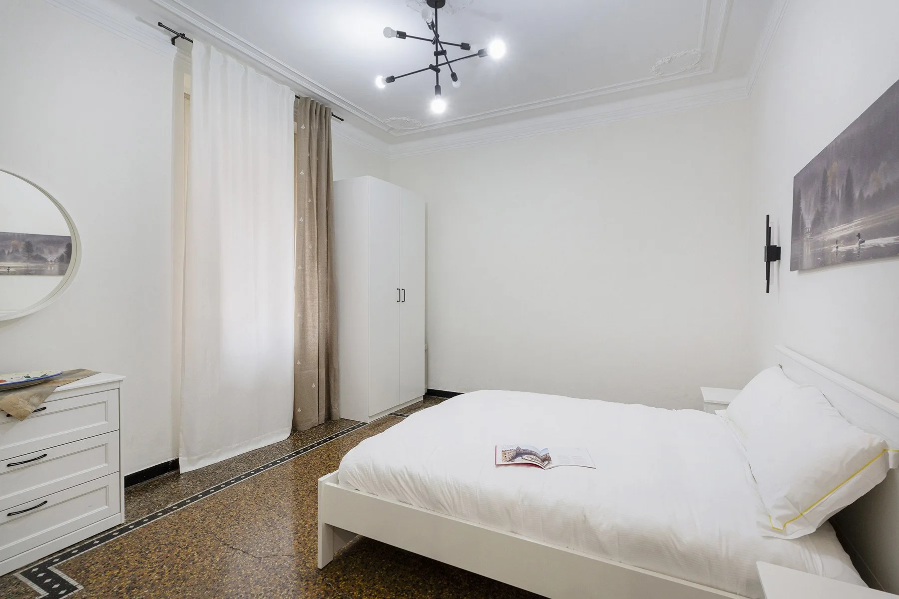Un dormitorio luminoso con una cama blanca, un armario y ventanas con cortinas.