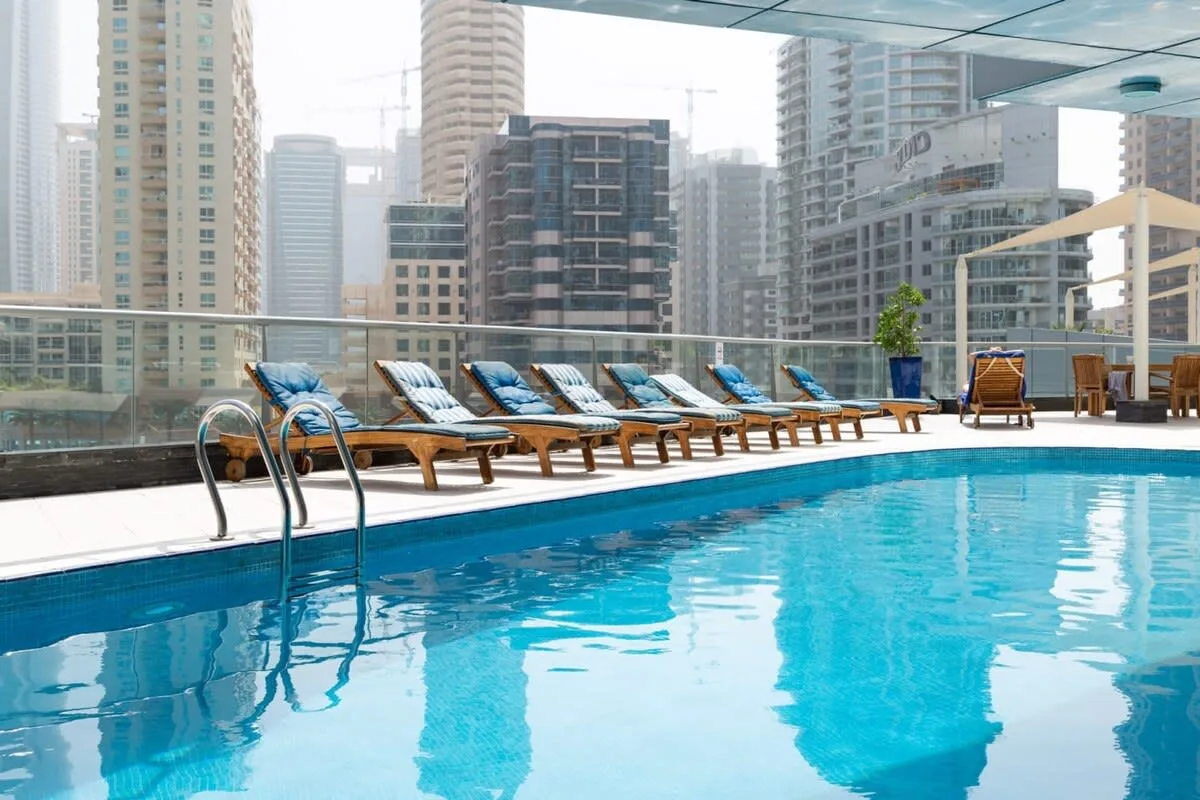 A rooftop pool with lounge seating overlooks a cluster of high-rise buildings.