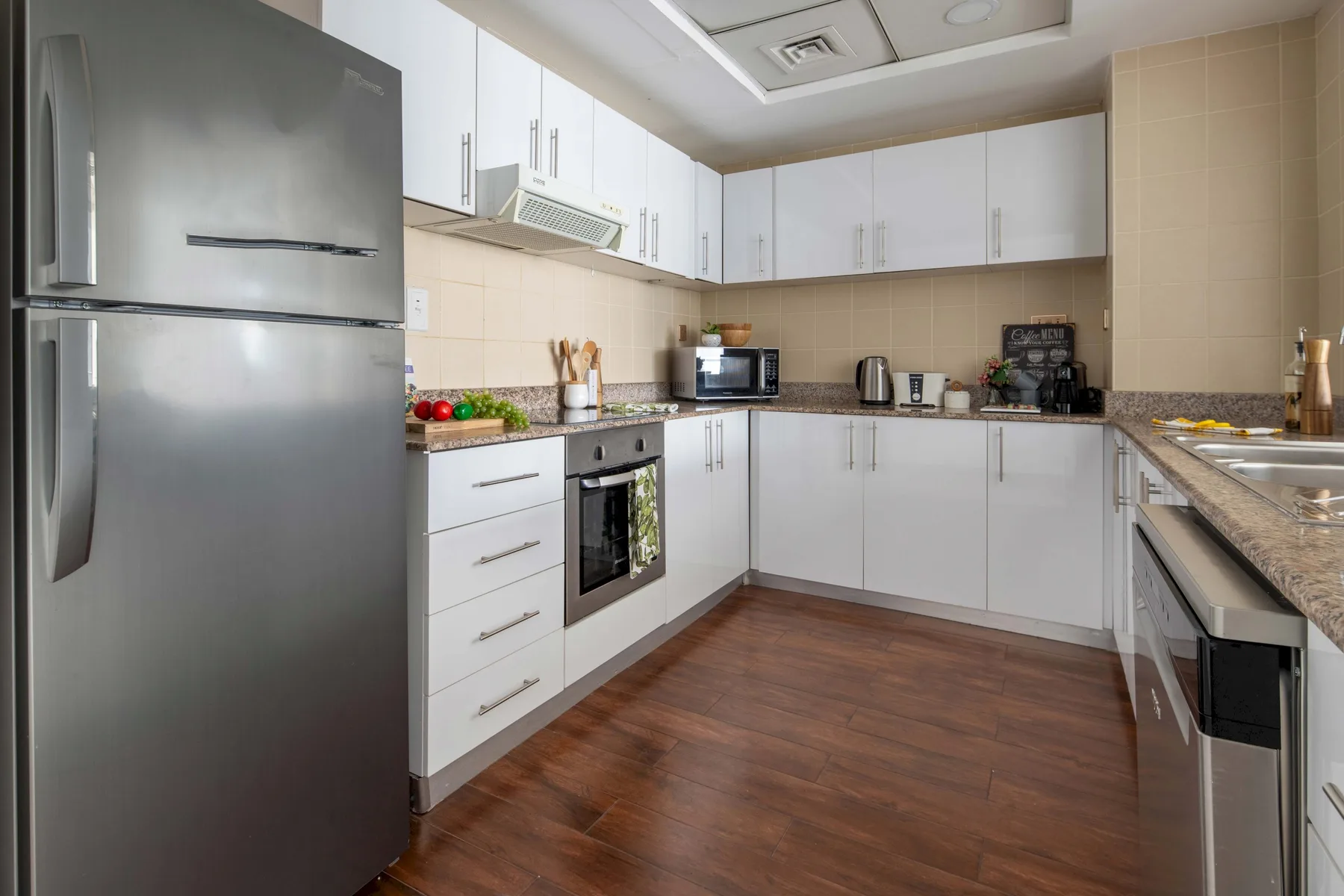 A modern kitchen with white cabinets, stainless steel appliances, and wood flooring.