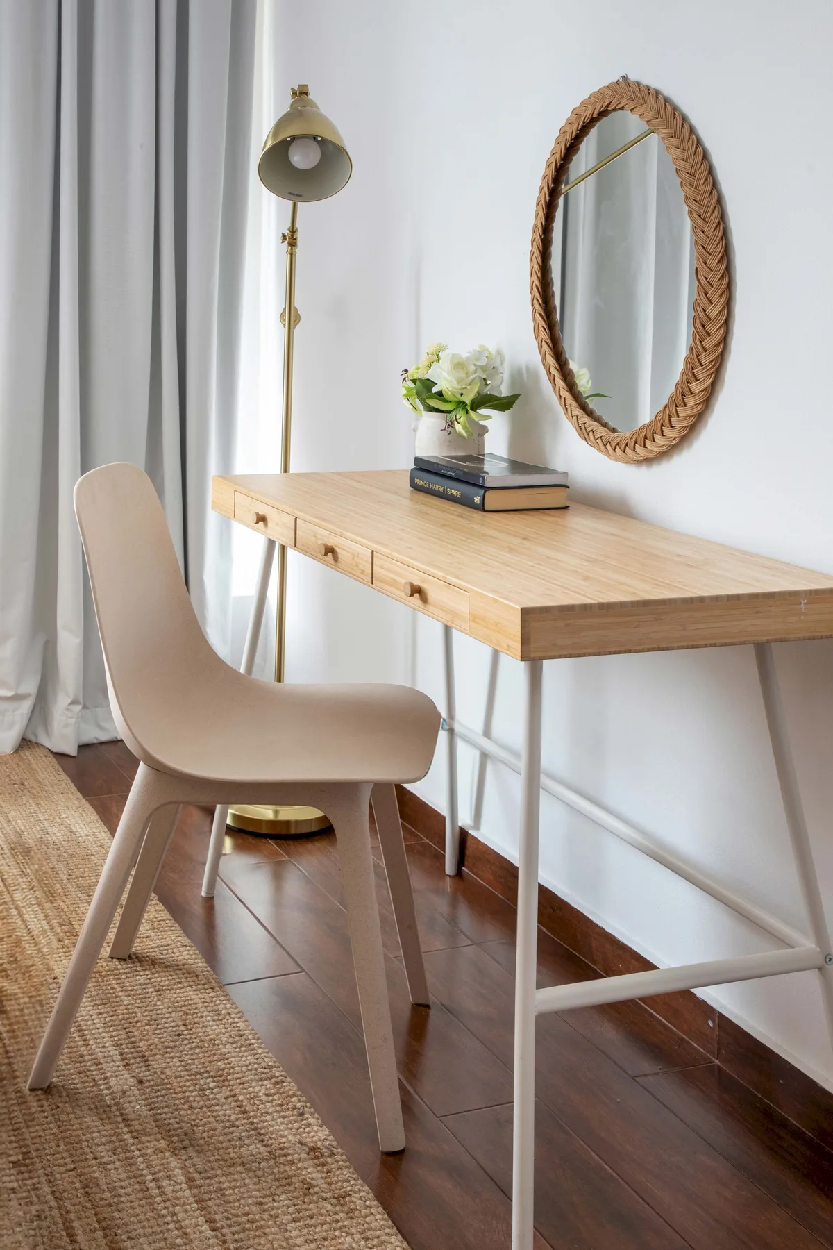 A bright desk area with a chair, floor lamp, and oval wall mirror.