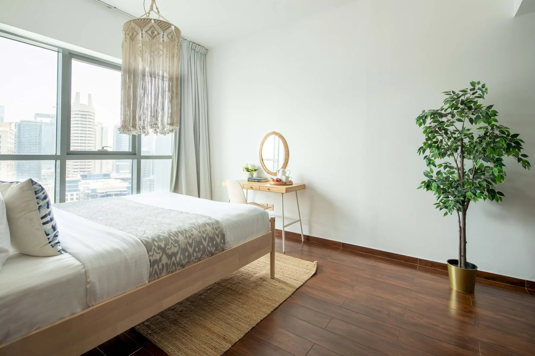 A bright bedroom with a bed beside large windows and a small vanity.