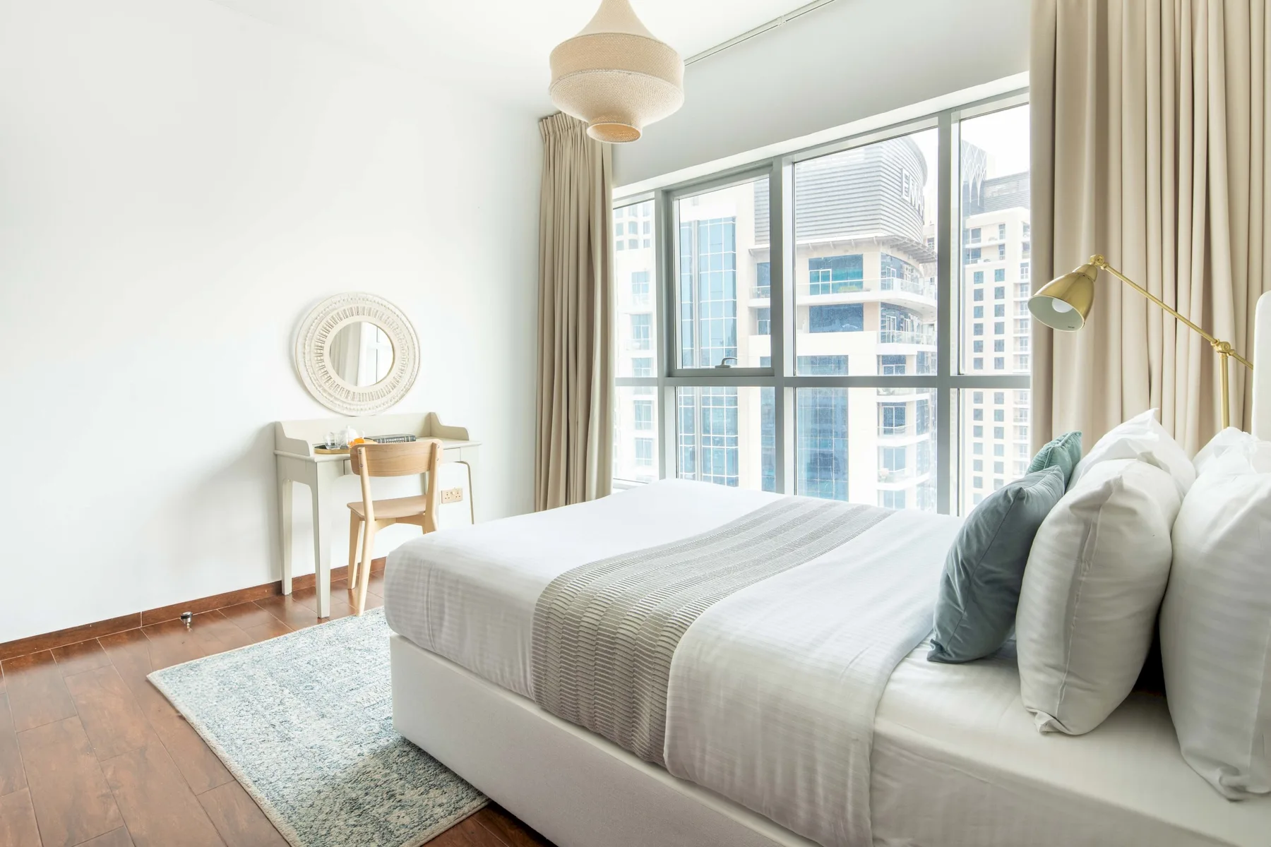 A bright bedroom with a neatly made bed beside large windows.