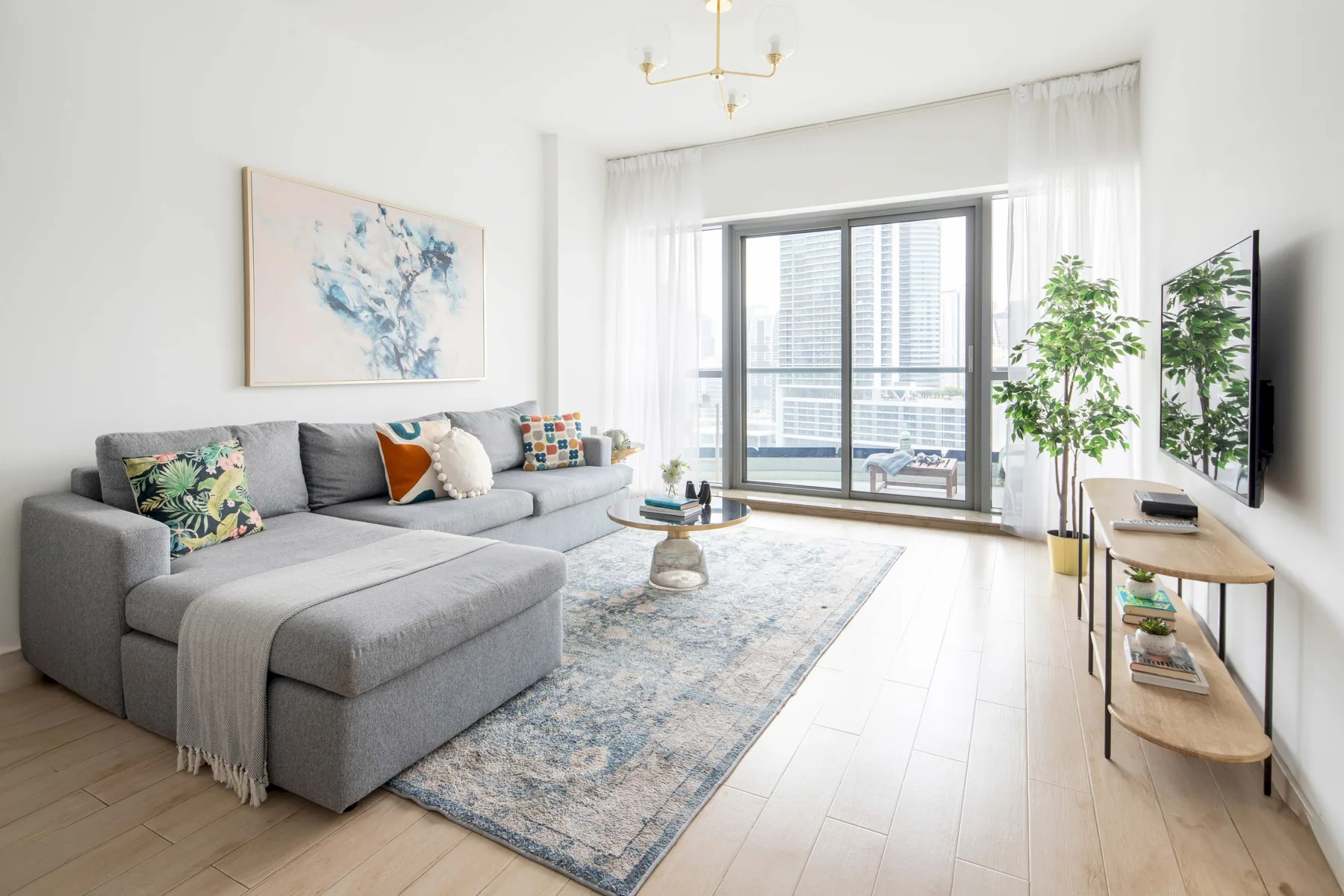 A bright living room with gray seating, a rug, and large windows.