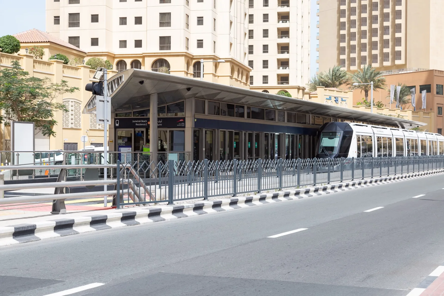 An elevated train station stands beside a road, with tall buildings in the background.