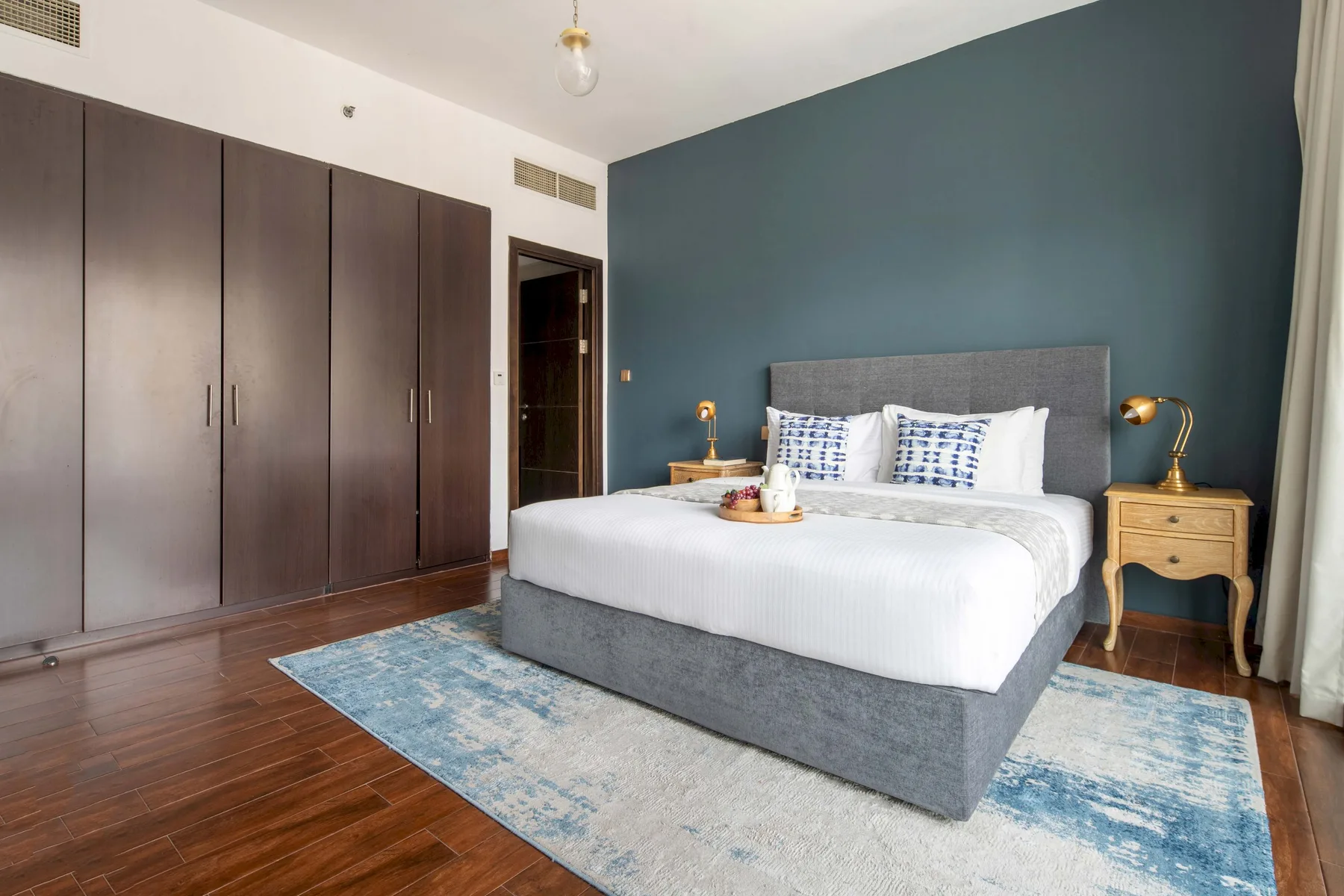 A bedroom with a bed against a dark teal wall and wardrobes along one side.