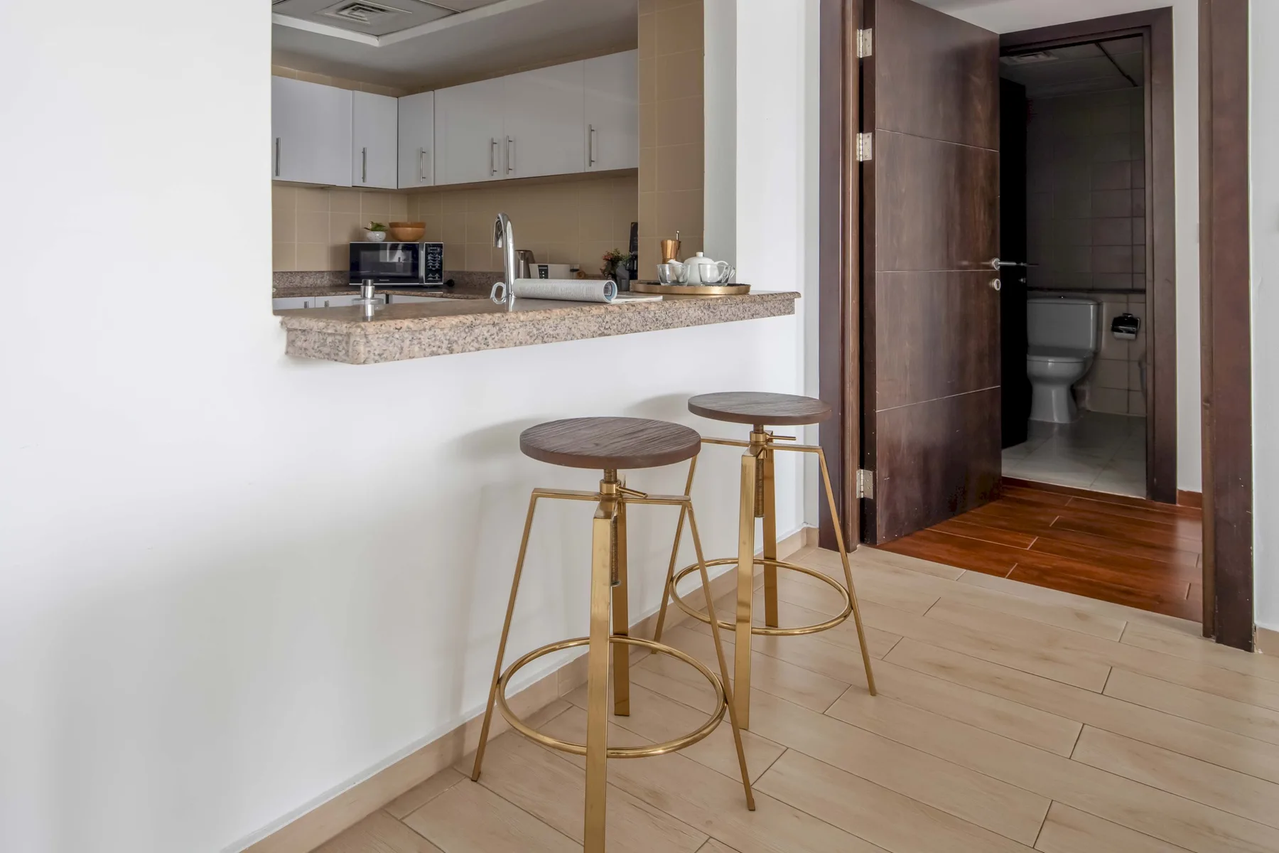 A kitchen counter with two stools sits beside an open doorway to a bathroom.