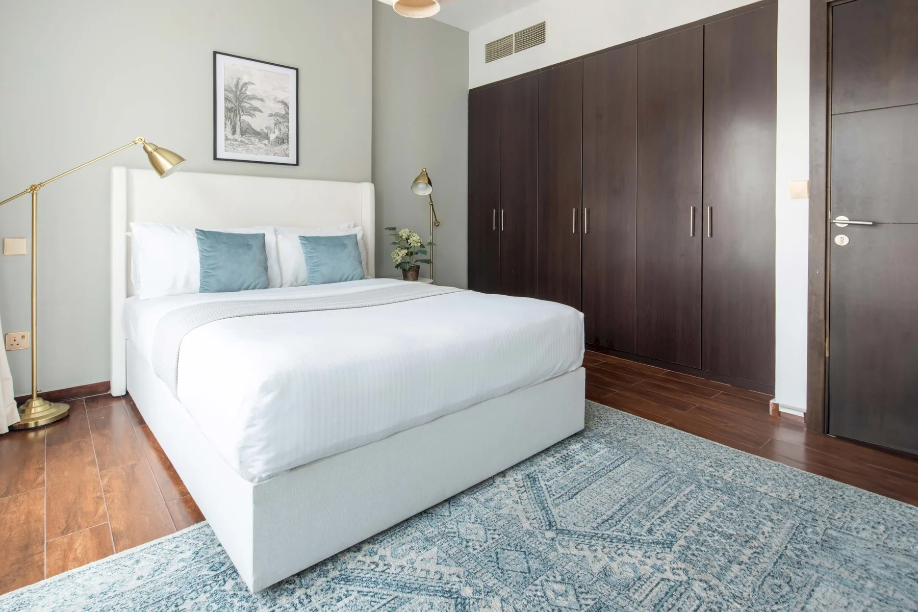 A bedroom with a neatly made bed, dark wardrobes, and a patterned rug.