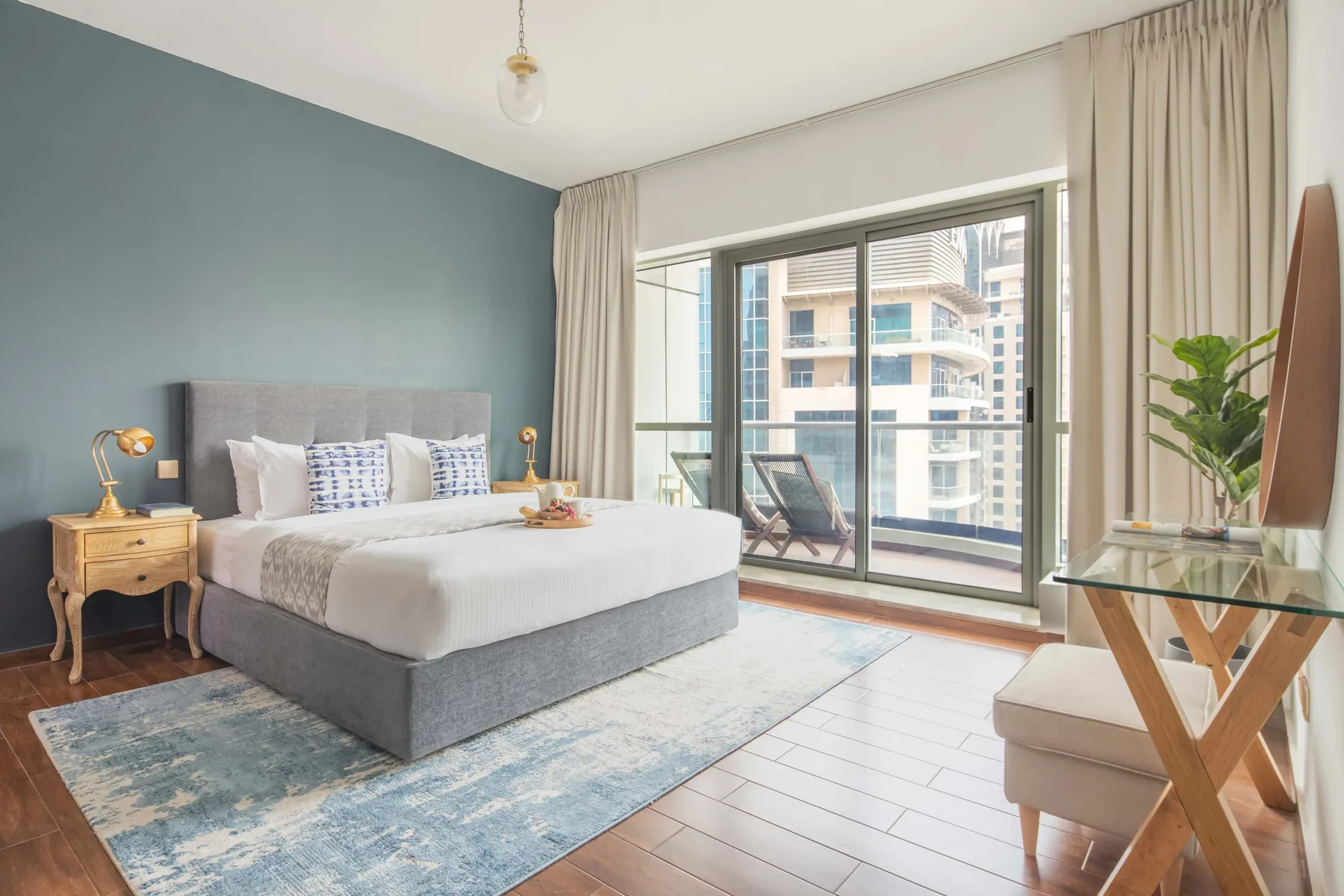 A bright bedroom with a large bed beside floor-to-ceiling windows.