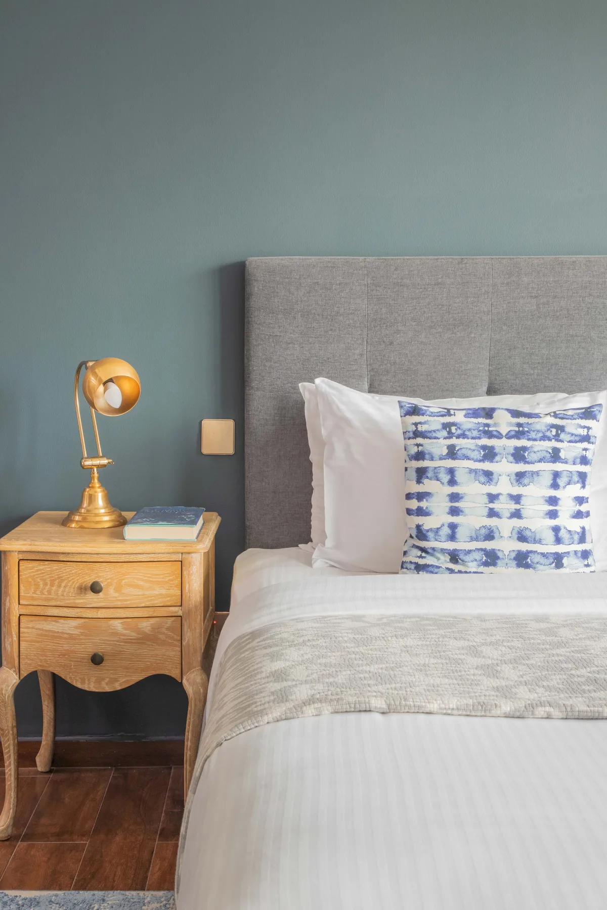 A bedroom with a neatly made bed and a wooden bedside table.