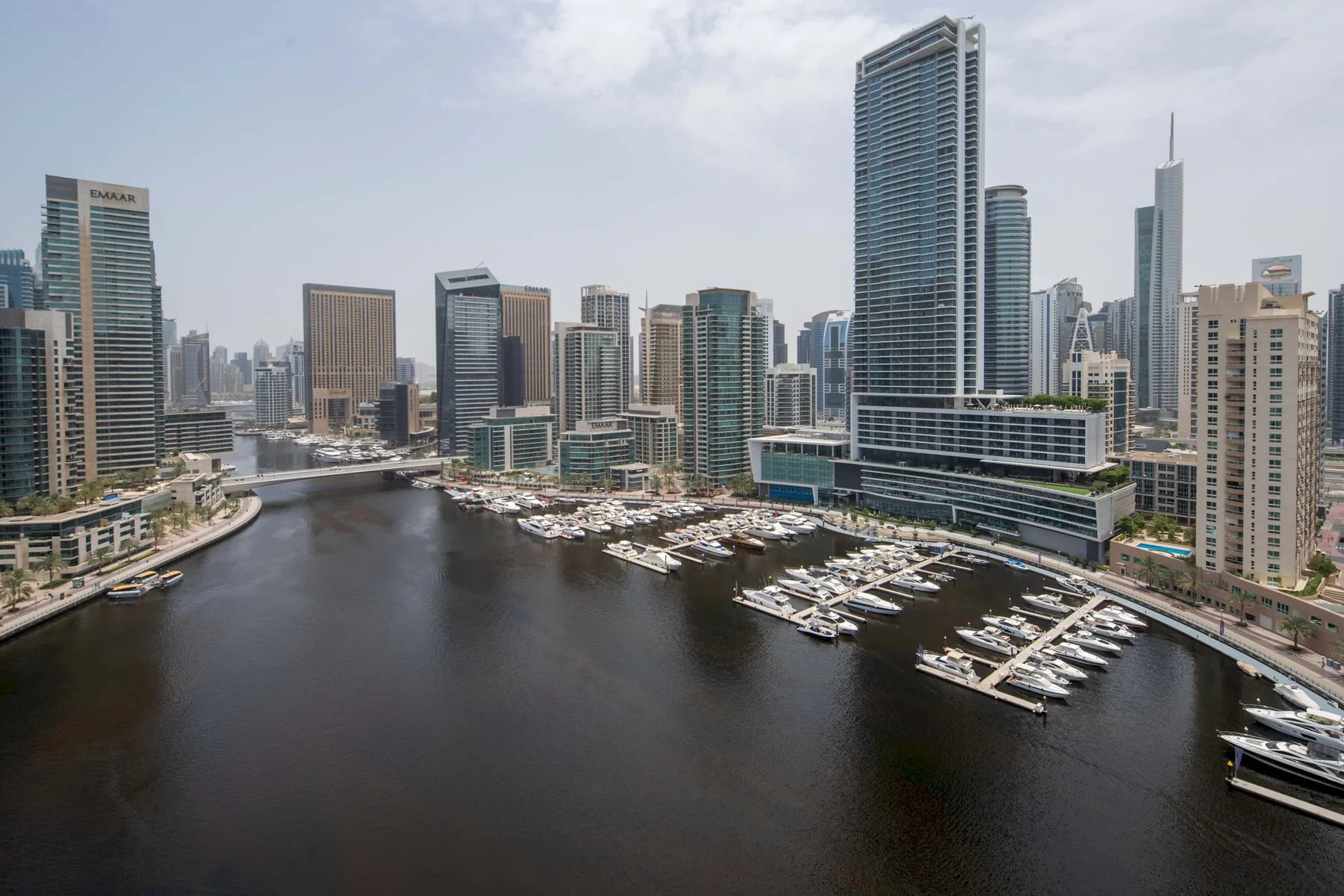 A waterfront marina with boats sits beneath a skyline of modern high-rise buildings.