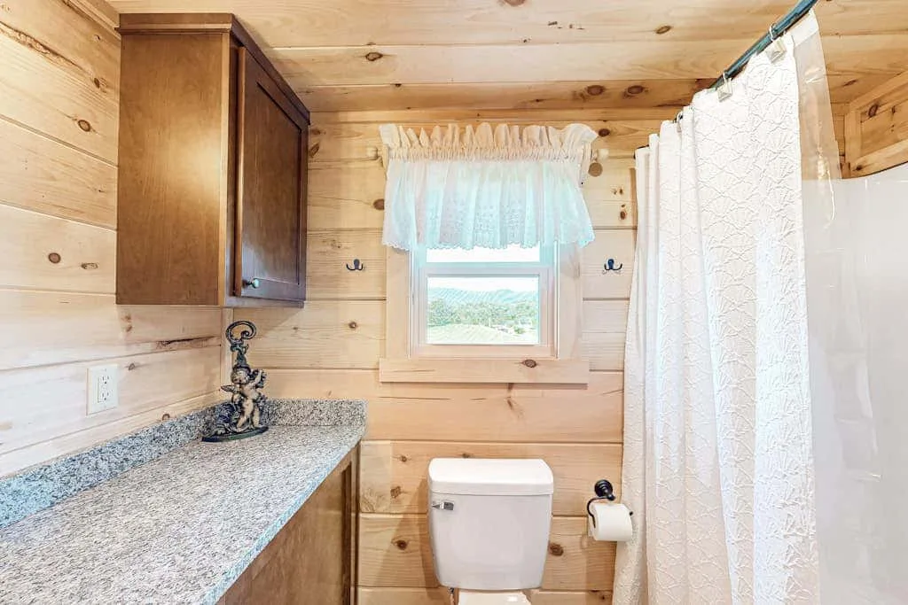 Baño revestido de madera con lavabo, inodoro y cortina de ducha.