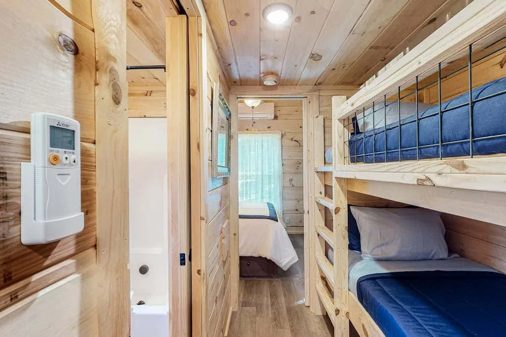 Una pequeña zona para dormir revestida de madera, con literas y una puerta hacia una cama.