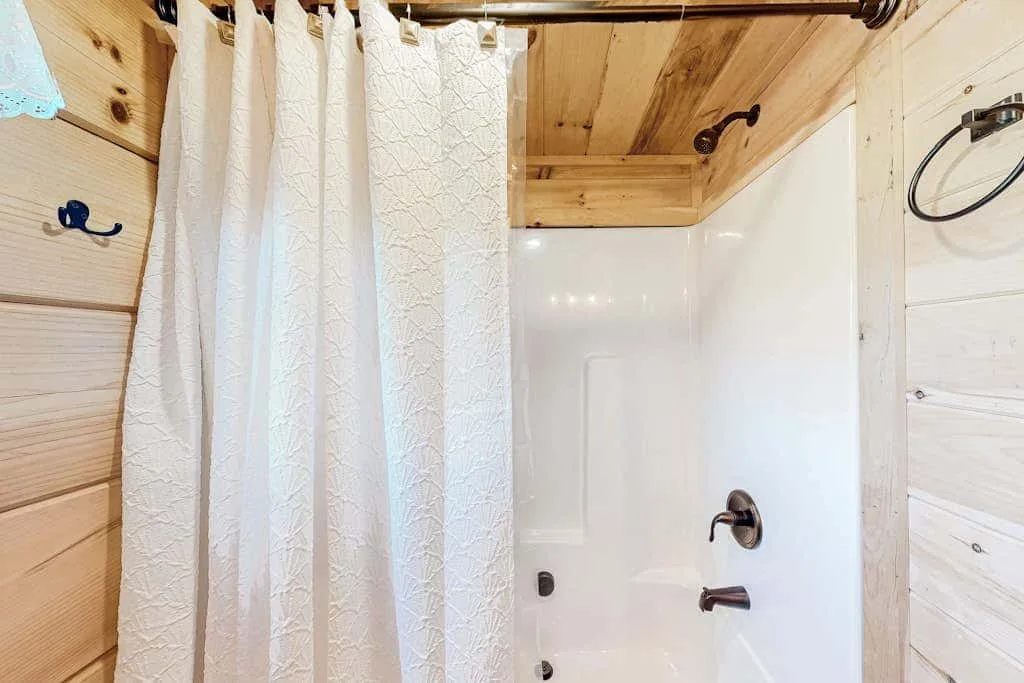 Un baño con ducha, cortina blanca y paredes revestidas de madera.