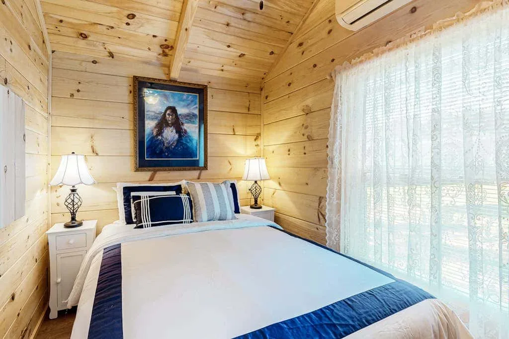 Un dormitorio con una cama bien arreglada y grandes ventanas con cortinas.