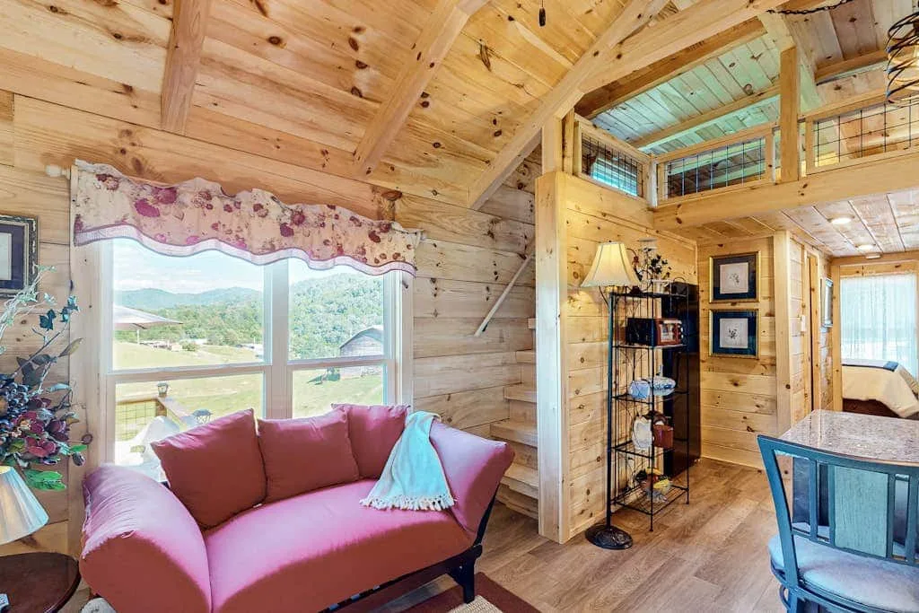 Una sala de estar revestida de madera con un sofá rosa junto a una ventana grande.