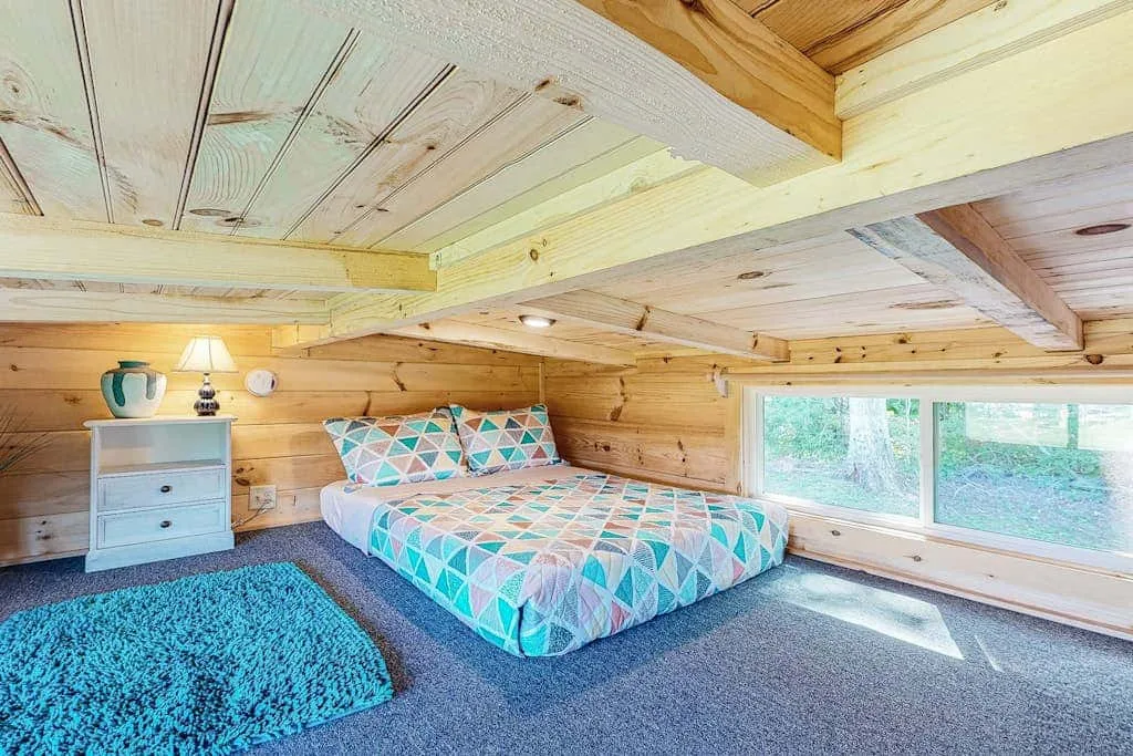 Un dormitorio revestido de madera con una cama junto a amplias ventanas.