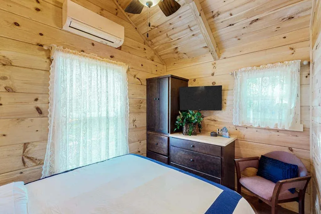 Un dormitorio revestido de madera con una cama, una cómoda y ventanas con cortinas.