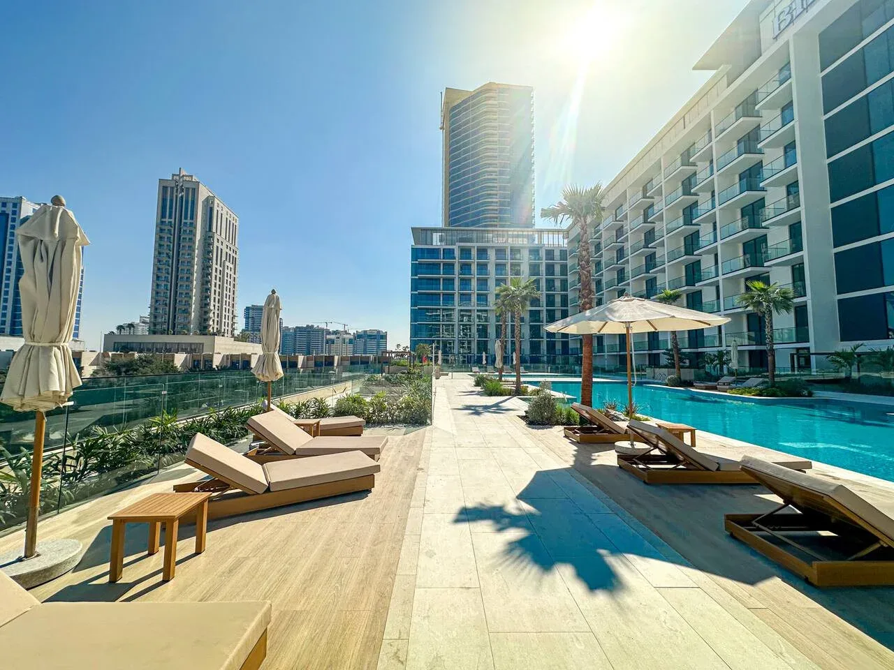 A rooftop pool deck with lounge seating overlooks modern high-rise buildings.
