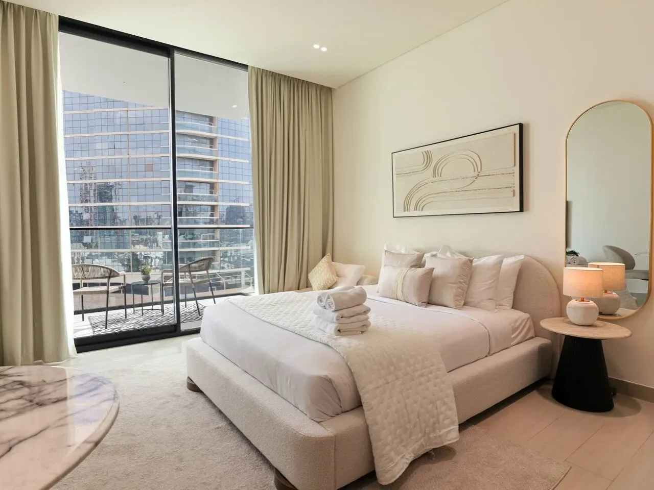 A bright bedroom with a large bed, bedside table, and floor-to-ceiling windows.