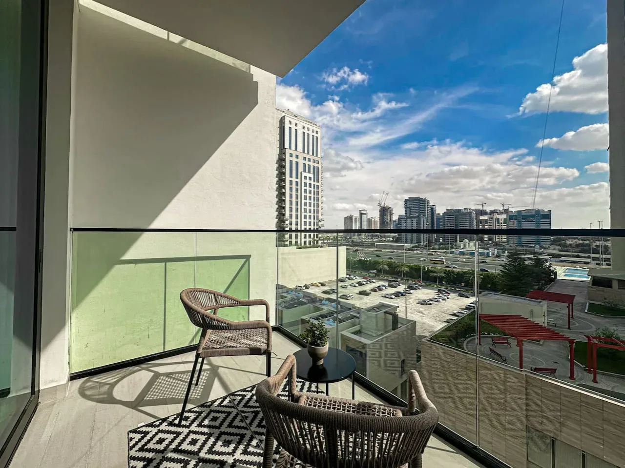 A balcony seating area overlooks nearby buildings beneath a bright blue sky.