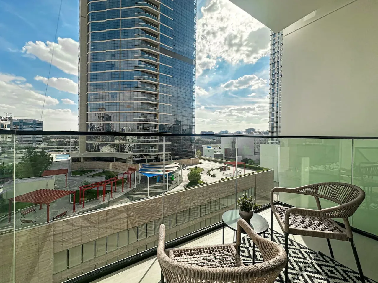 A balcony seating area overlooks a modern cityscape through glass railings.