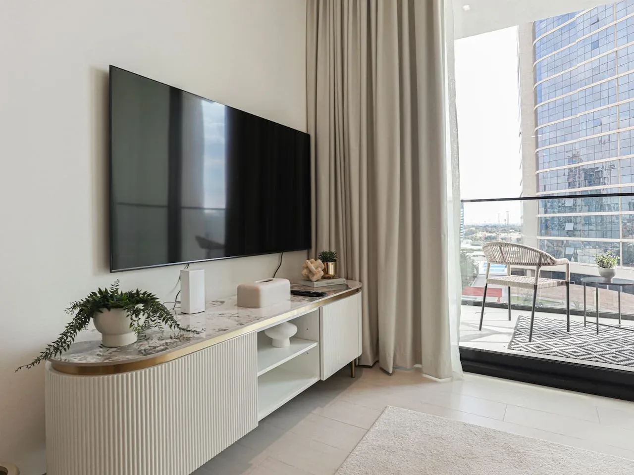 A bright living area with a television above a low console beside a glass balcony door.
